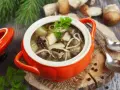 Aromatyczna zupa grzybowa ze świeżych grzybów, podana w pomarańczowym naczyniu, z gałązką natki pietruszki.