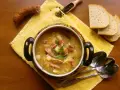 Aromaticzny kapuśniak z kiszonej kapusty, podany w ozdobnym garnku, z kiełbasą, ziemniakami i pieczywem.