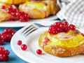 Pyszne drożdżówki z budyniem, ozdobione świeżymi czerwonymi porzeczkami, kuszą na białym talerzyku.