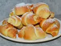 Stos świeżo upieczonych rogalików z czekoladą, posypanych cukrem pudrem, na talerzu.