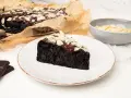 Wilgotny brownie z buraka, polany czekoladą i posypany płatkami migdałów, na talerzu.
