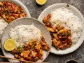 Dwa talerze z kurczakiem teriyaki i makaronem ryżowym, udekorowane plasterkami limonki i szczypiorkiem.