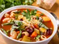 A miseczce aromatyczna zupa minestrone, oryginalny przepis z makaronem, fasolką, ziemniakami i startym parmezanem.