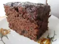 Wilgotne ciasto czekoladowe z dżemem porzeczkowym, posypane cukrem pudrem, na talerzyku z motywem kwiatowym.