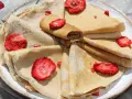 Stos cienkich naleśników z truskawkami na talerzu.