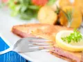 Smażony kotlet z mortadeli, podany z ziemniakami, sałatką i plasterkiem cytryny z natką pietruszki.