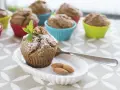 Pyszne muffinki bananowe fit, posypane cukrem pudrem, z orzechami i miętą. Obok migdały i łyżeczka.