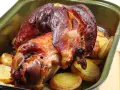 Pieczona golonka w zielonej brytfance, otoczona ziemniakami. Idealna marynata do golonki sprawiła, że skórka jest chrupiąca.