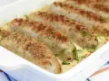 Pieczona biała kiełbasa w kremowym sosie chrzanowym, udekorowana świeżym koperkiem. Pyszne danie gotowe do podania.