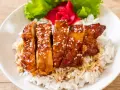 Pyszny kurczak w miodzie, polany sosem teriyaki i posypany sezamem, podany na ryżu z dodatkiem sałaty i marynowanego imbiru.