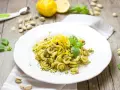 Makaron z zielonym pesto, którego głównym składnikiem są pistacje, ozdobiony skórką cytrynową i listkami bazylii.