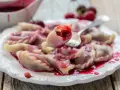 Pyszne pierogi z wiśniami, polane słodkim sosem, kuszą swoim wyglądem. Jedna sztuka jest podniesiona widelcem, ukazując soczyste nadzienie.