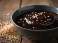Gęsty, błyszczący sos teriyaki w misce, posypany sezamem. Obok garść ziaren sezamu. Idealny sos teriyaki przepis.