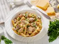 Makaron z tuńczykiem z puszki, groszkiem i pieczarkami w kremowym sosie, posypany natką pietruszki. Obok kawałki parmezanu i tarka.