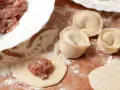Przygotowanie pierogów z mięsem mielonym surowym. Na drewnianej desce widać surowe ciasto, farsz i gotowe pierożki.
