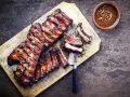 Soczyste żeberka w miodzie, grillowane do perfekcji, podane na desce z sosem.