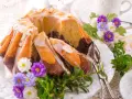 Modne ciasta na Wielkanoc: marmurkowa babka z lukrem i migdałami, ozdobiona wiosennymi kwiatami i zielenią.