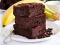 Stos puszystych brownie z bananami, ozdobiony ziarnami kawy, na talerzu z bananem w tle.