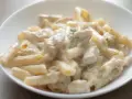 Penne w kremowym sosie serowym z kawałkami kurczaka, udekorowane gałązką ziół. Pyszny makaron serowy z kurczakiem.