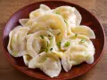 Pyszne pierogi z tradycyjnym farszem do uszek, posypane szczypiorkiem, na glinianym talerzu.