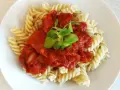 Fusilli z sosem pomidorowym i pomidorkami koktajlowymi, udekorowane świeżą zieleniną. Pyszne danie gotowe w kilka minut.