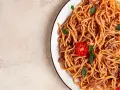 Talerz spaghetti bolognese z pomidorkiem i bazylią na jasnym tle.
