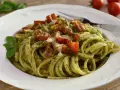 Pyszny makaron z pesto, pomidorkami i parmezanem, udekorowany listkiem bazylii. Idealny na szybki obiad.