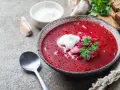 Najprostsza zupa buraczkowa, gorąca, z kleksem śmietany i natką pietruszki, obok czosnek i chleb.