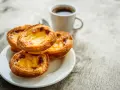 Na talerzyku leżą trzy chrupiące pastéis de nata, obok filiżanka kawy. Idealny poranek.