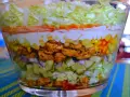 Warstwowa sałatka z kurczakiem w stylu gyros, z kukurydzą, ogórkiem, cebulą i sosem.