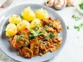 Gulasz drobiowy z pieczarkami i ziemniakami na talerzu, ozdobiony natką pietruszki.