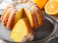 Puszysta babka na oleju, oprószona cukrem pudrem, z pomarańczami w tle. Idealna na niedzielne popołudnie.