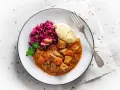 Gulasz wieprzowy z warzywami, podany z purée ziemniaczanym i czerwoną kapustą. Pyszne danie obiadowe.