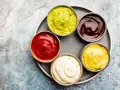Sześć miseczek z sosami: zielony guacamole, czerwony ketchup, ciemny barbecue, żółta musztarda i biały majonez. Idealne do dań, gdy zastanawiasz się, jak zrobić sos.