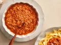 Gęsty, aromatyczny sos do spaghetti bolognese w miseczce, obok porcji makaronu tagliatelle.