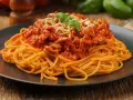 Pyszne spaghetti z mięsem mielonym, polane sosem pomidorowym i posypane startym serem, ozdobione listkiem bazylii.