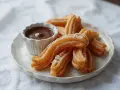Churros con chocolate, złociste, posypane cukrem, czekają na zanurzenie w gorącej, gęstej czekoladzie. Idealna przekąska.