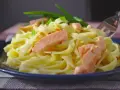 Pyszny makaron z łososiem, udekorowany szczypiorkiem, czeka na widelcu.