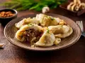 Talerz pełen pysznych, domowych pierogów z kapustą i grzybami, posypanych szczypiorkiem. Obok czosnek i pieprz.