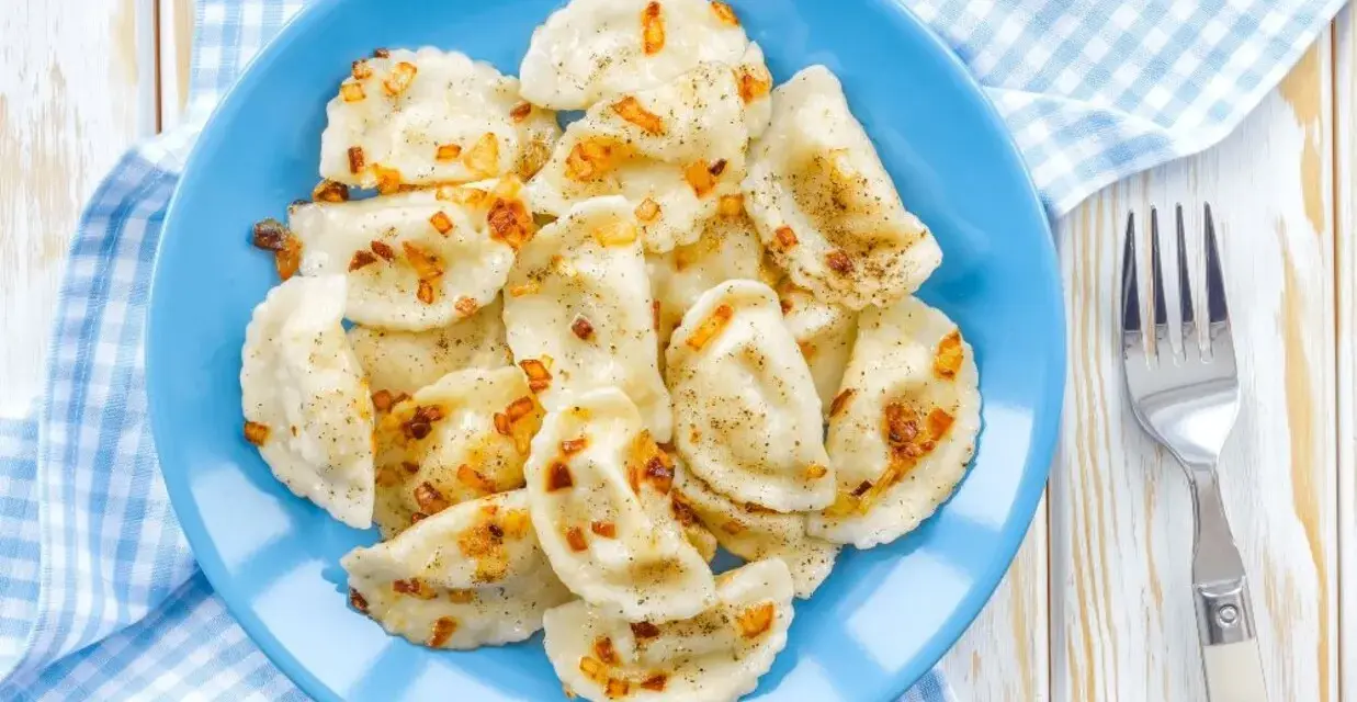 Pyszne pierogi z soczewicą czerwoną, posypane skwarkami i pieprzem, na niebieskim talerzu.