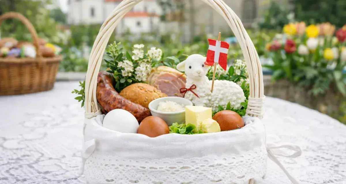Biały koszyk z tradycyjnymi produktami co do swieconki: jajka, kiełbasa, chleb, masło, baranek z flagą Danii.