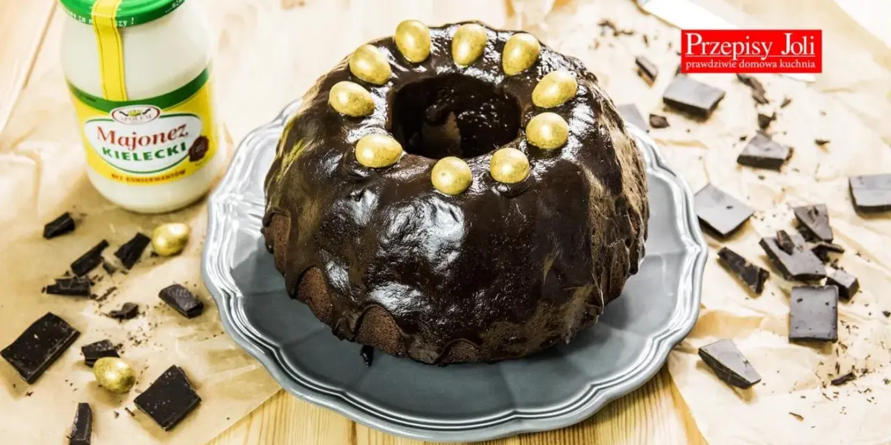 Babka majonezowa z przepisów Joli, polana czekoladą i ozdobiona złotymi jajeczkami. Obok słoik majonezu i kawałki czekolady.