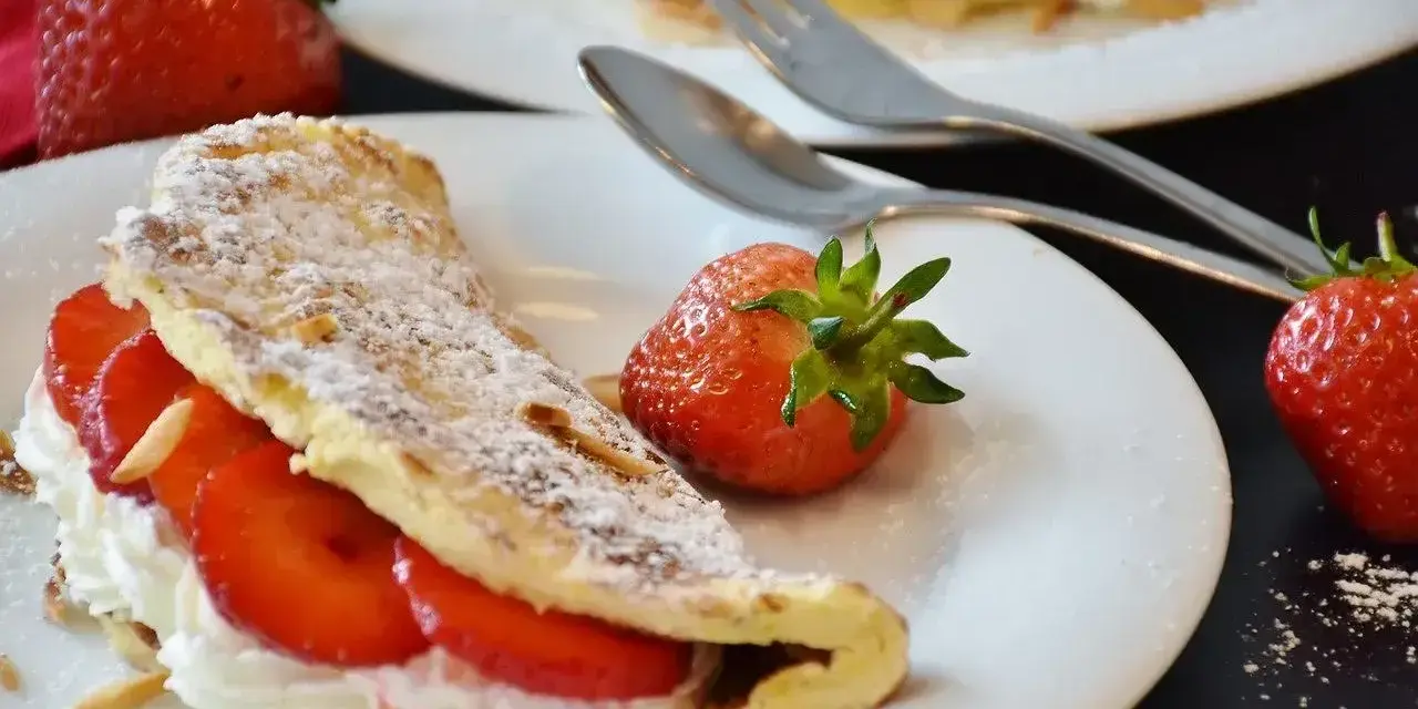 Słodki omlet z bitą śmietaną i truskawkami, posypany cukrem pudrem i płatkami migdałów. Idealny deser na słodko.