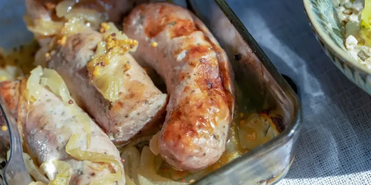 Biała kiełbasa pieczona z cebulką i musztardą w szklanym naczyniu. Apetyczny zapach unosi się w powietrzu.