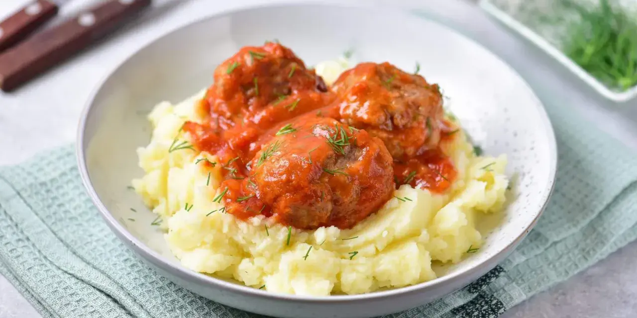 Pyszne pulpeciki w sosie pomidorowym na kremowym purée ziemniaczanym, posypane świeżym koperkiem.