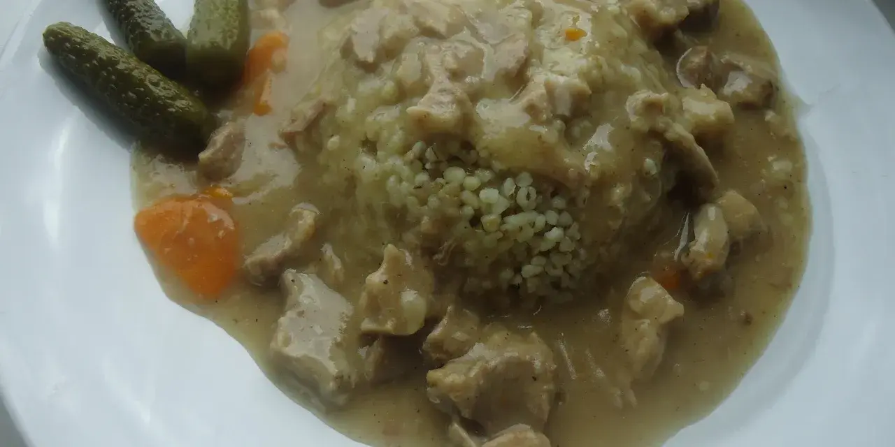 Gulasz z kaszą, podany z ogórkami kiszonymi i marchewką. Aromatyczne mięso w sosie, idealnie komponuje się z puszystą kaszą.