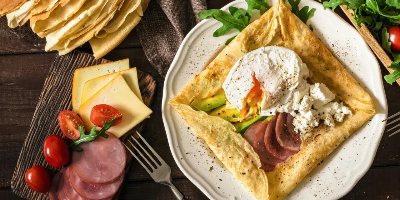 Naleśniki po francusku z jajkiem w koszulce, awokado, szynką i serem. Pyszne śniadanie.