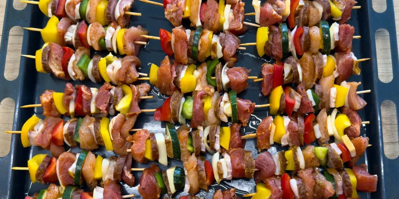 Szaszłyki w piekarniku gotowe do pieczenia: mięso, papryka, cebula i cukinia na patyczkach.