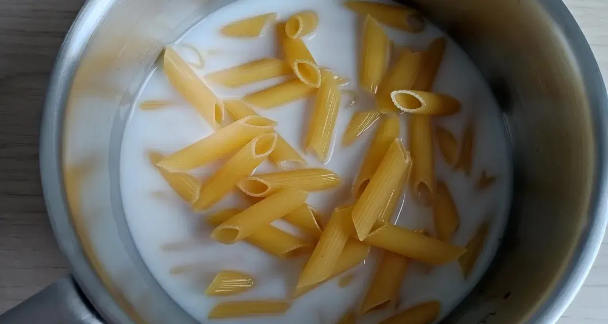 Makaron penne gotuje się w mleku w metalowym garnku.