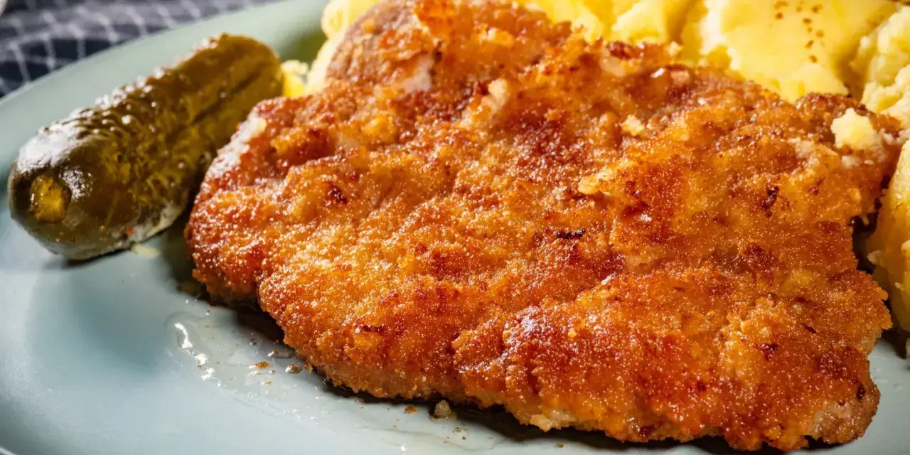 Chrupiące kotlety z karkówki, purée ziemniaczane i ogórek kiszony na talerzu.